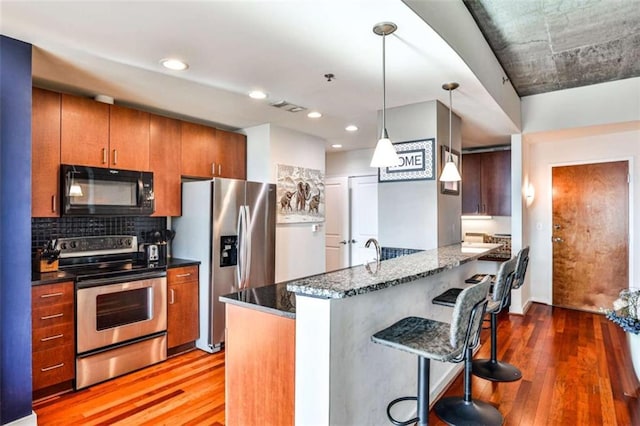 kitchen featuring stainless steel appliances, decorative light fixtures, a kitchen bar, dark stone countertops, and hardwood / wood-style floors