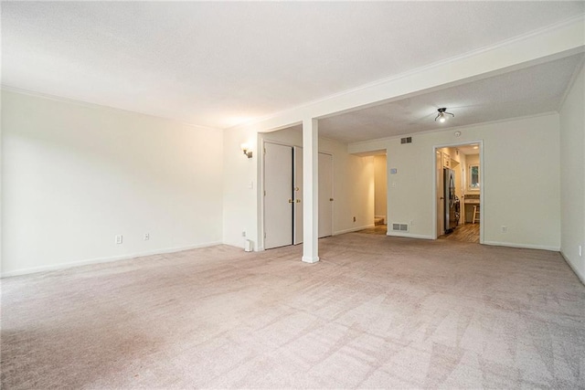 spare room with light carpet, baseboards, visible vents, and crown molding