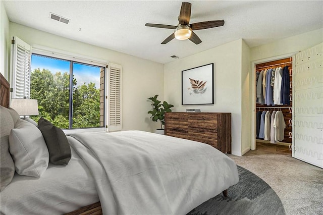 bedroom featuring ceiling fan, light colored carpet, visible vents, a closet, and a walk in closet