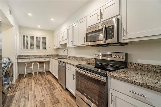 kitchen featuring stainless steel appliances, white cabinetry, a sink, separate washer and dryer, and light wood-type flooring