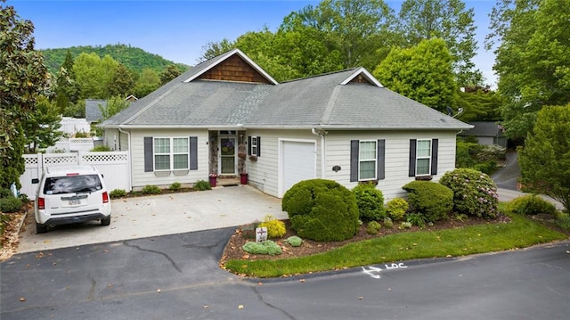 view of front facade with fence, an attached garage, a shingled roof, and driveway