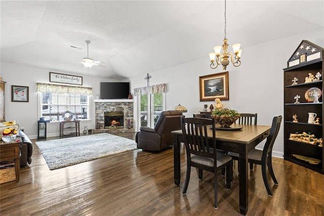 dining area featuring ceiling fan with notable chandelier, vaulted ceiling, a fireplace, dark wood-style floors, and baseboards
