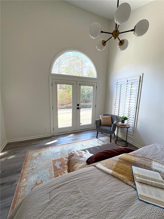 bedroom with an inviting chandelier, wood finished floors, a high ceiling, access to outside, and french doors