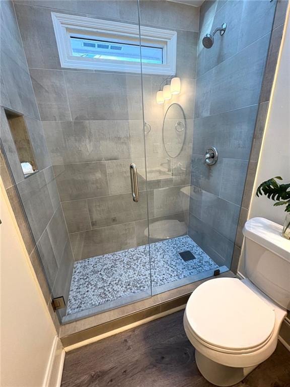 bathroom with toilet, wood finished floors, and a stall shower