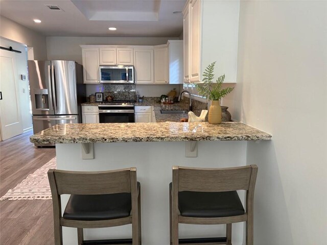 kitchen featuring visible vents, a sink, a peninsula, stainless steel appliances, and white cabinetry