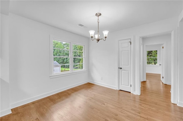 spare room featuring plenty of natural light, an inviting chandelier, and light hardwood / wood-style floors