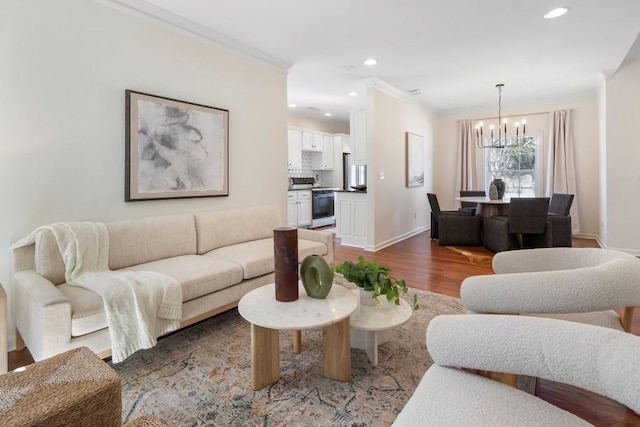 living room with wood finished floors, recessed lighting, an inviting chandelier, crown molding, and baseboards