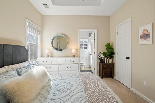 bedroom with visible vents, a tray ceiling, connected bathroom, baseboards, and light colored carpet