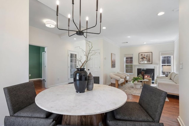 dining area featuring a glass covered fireplace, recessed lighting, ornamental molding, and wood finished floors