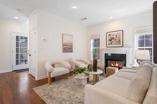 living room with dark wood finished floors, a glass covered fireplace, crown molding, and visible vents