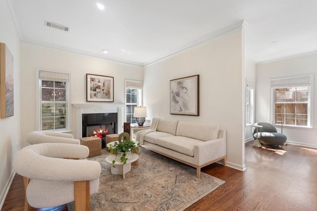 living room featuring visible vents, wood finished floors, a glass covered fireplace, and crown molding