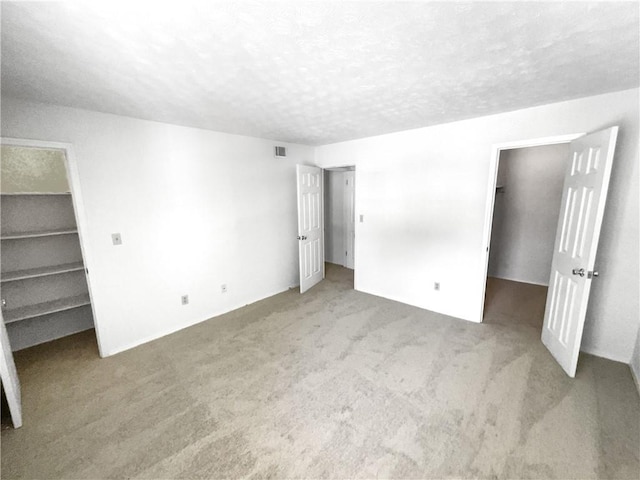 unfurnished bedroom featuring a textured ceiling, a spacious closet, a closet, and carpet floors