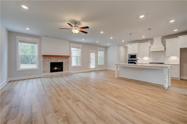 unfurnished living room featuring a brick fireplace, ceiling fan, sink, and light wood-type flooring