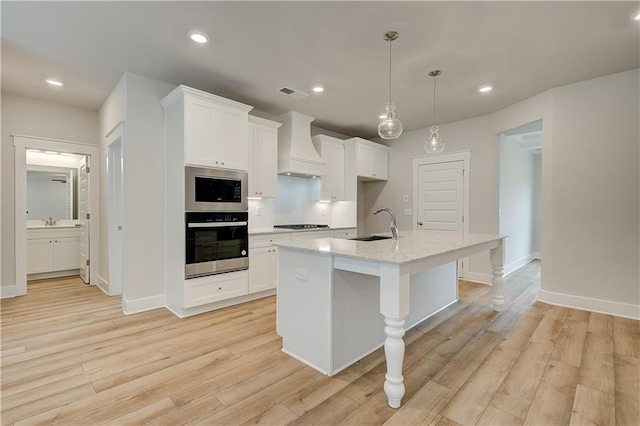 kitchen featuring custom exhaust hood, a kitchen island with sink, pendant lighting, light hardwood / wood-style flooring, and white cabinetry