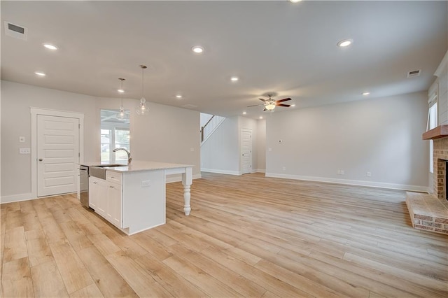 kitchen featuring a brick fireplace, ceiling fan, decorative light fixtures, white cabinets, and an island with sink