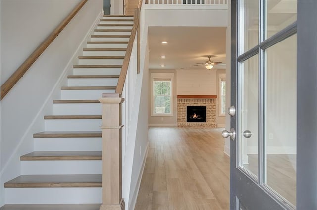 staircase with ceiling fan, wood-type flooring, and a fireplace