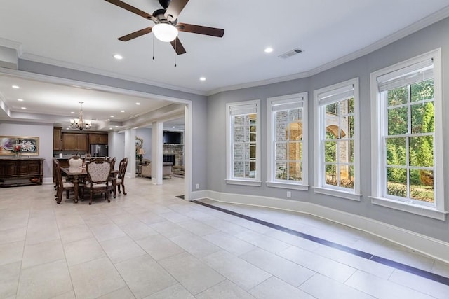 tiled dining room featuring ceiling fan with notable chandelier, crown molding, and a stone fireplace