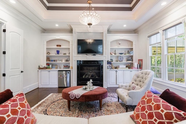 living room featuring built in features, an inviting chandelier, crown molding, a tray ceiling, and dark hardwood / wood-style flooring