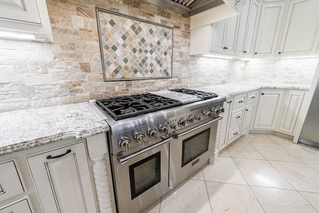 kitchen with light stone counters, white cabinets, double oven range, and backsplash