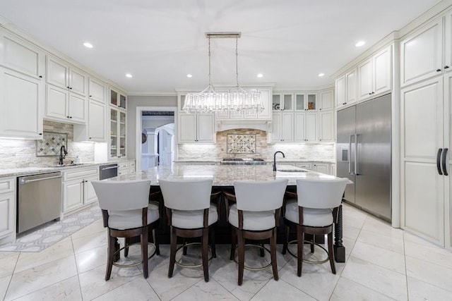 kitchen with decorative backsplash, sink, appliances with stainless steel finishes, decorative light fixtures, and a center island with sink