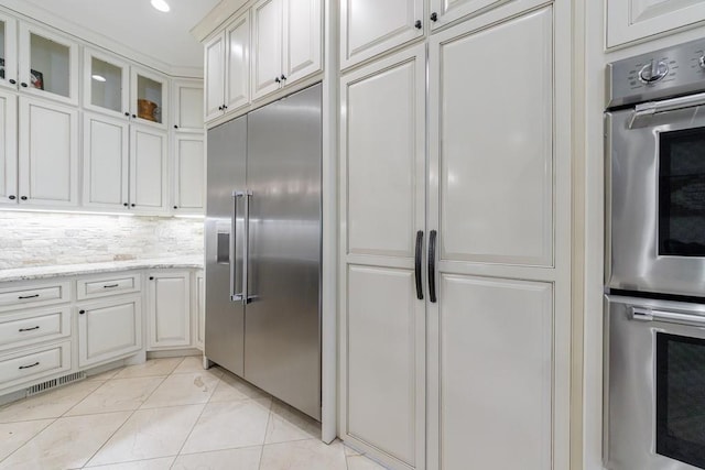 kitchen with light stone counters, decorative backsplash, white cabinetry, appliances with stainless steel finishes, and light tile patterned floors