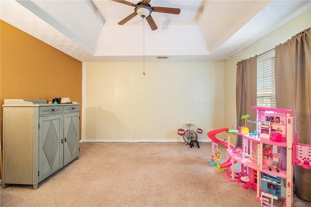 playroom featuring ceiling fan, light colored carpet, and a tray ceiling