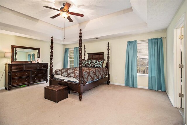 bedroom featuring light carpet, a tray ceiling, and ceiling fan