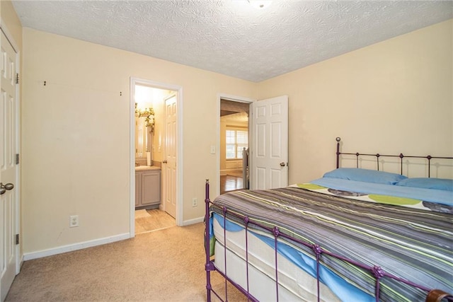 bedroom featuring light colored carpet, a textured ceiling, and connected bathroom