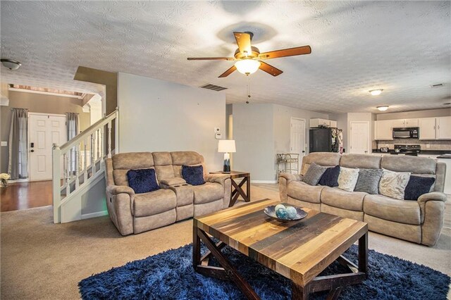 living room featuring ceiling fan, light colored carpet, and a textured ceiling