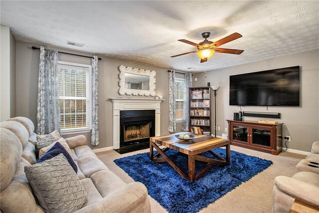 living room featuring ceiling fan, light colored carpet, and a textured ceiling