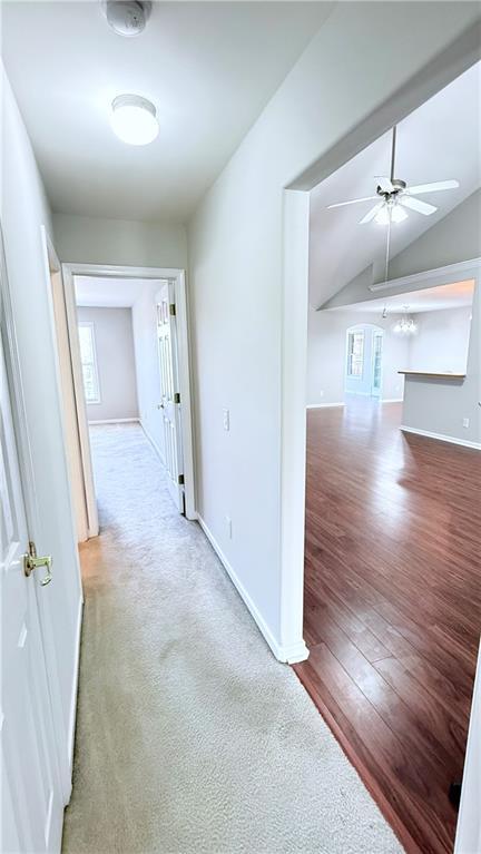 hall with carpet flooring, vaulted ceiling, baseboards, and wood finished floors