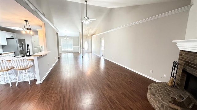 living room featuring a brick fireplace, baseboards, dark wood-style flooring, and ceiling fan with notable chandelier