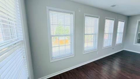 spare room with visible vents, baseboards, dark wood-style flooring, and a wealth of natural light