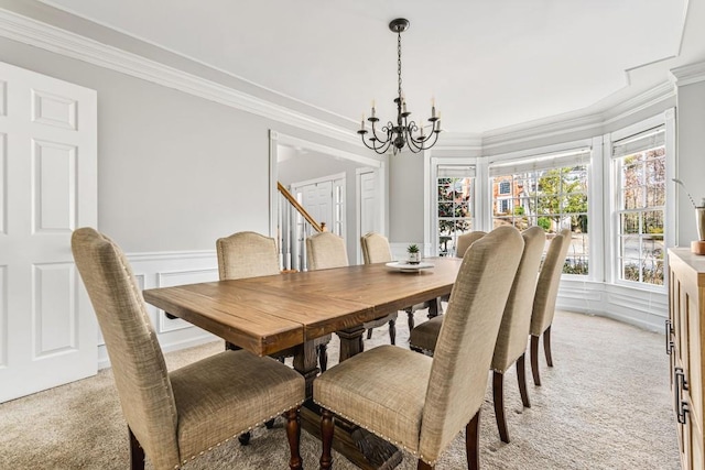dining room with a notable chandelier, a decorative wall, crown molding, a wainscoted wall, and light carpet