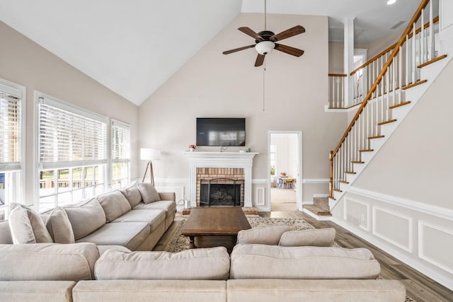 living area featuring wood finished floors, high vaulted ceiling, a wainscoted wall, ceiling fan, and stairs