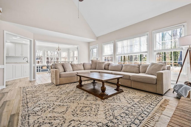 living area featuring a notable chandelier, light wood finished floors, high vaulted ceiling, and plenty of natural light