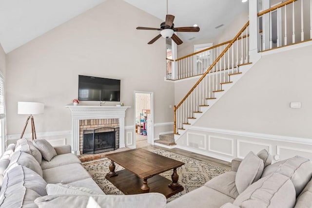 living area featuring a ceiling fan, stairway, a decorative wall, and high vaulted ceiling