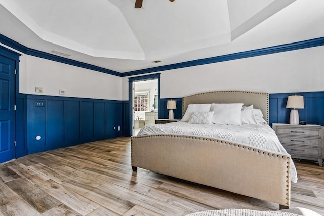 bedroom featuring a ceiling fan, a tray ceiling, wainscoting, visible vents, and wood finished floors