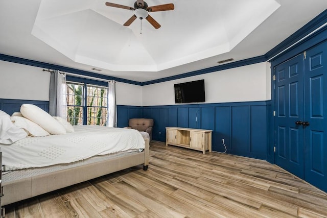 bedroom featuring a raised ceiling, a wainscoted wall, visible vents, and wood finished floors