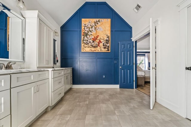 bathroom featuring double vanity, lofted ceiling, a decorative wall, and visible vents