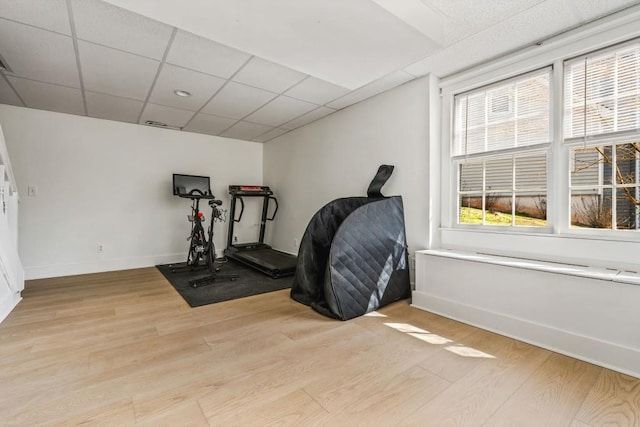 exercise room featuring baseboards, light wood-style flooring, and a paneled ceiling