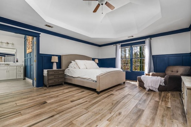 bedroom with wainscoting, a raised ceiling, a decorative wall, and visible vents