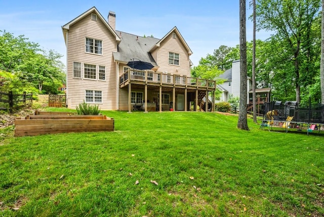rear view of property featuring a trampoline, a wooden deck, a garden, and fence