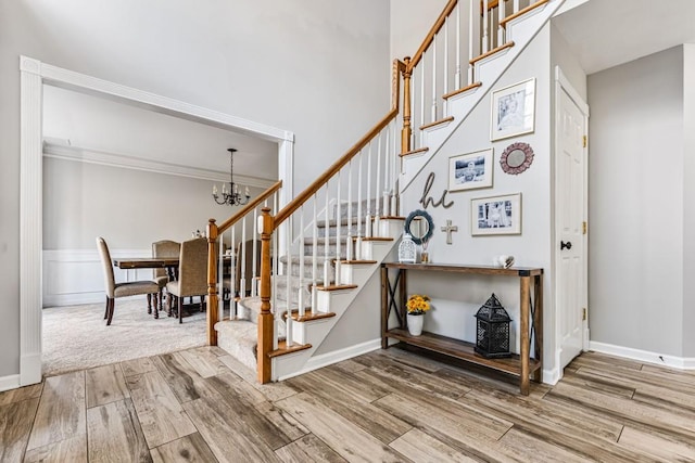 stairway with ornamental molding, a notable chandelier, baseboards, and wood finished floors
