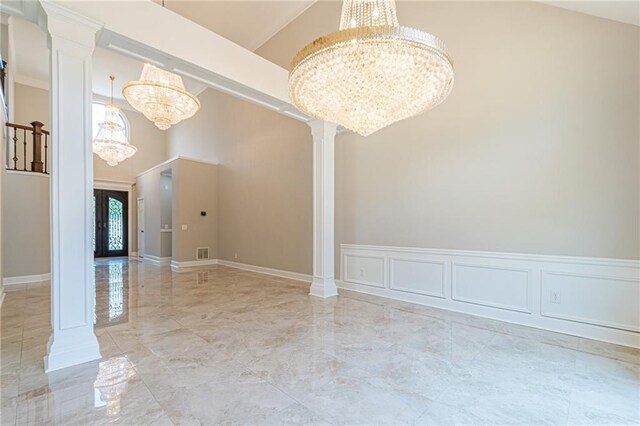 unfurnished room with ornate columns, french doors, a towering ceiling, and a notable chandelier