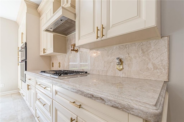 kitchen featuring stainless steel gas stovetop, backsplash, premium range hood, light stone countertops, and double oven