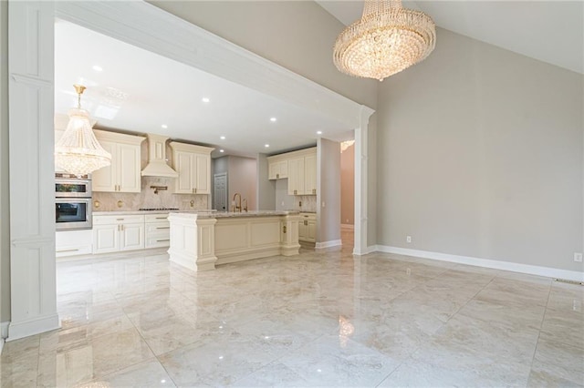 kitchen featuring decorative backsplash, custom exhaust hood, cooktop, stainless steel double oven, and a chandelier