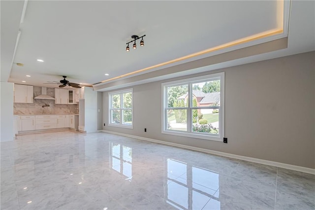 unfurnished living room with ceiling fan and a raised ceiling