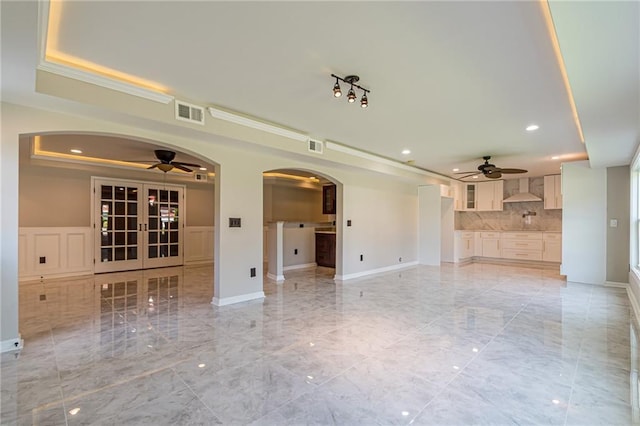 unfurnished living room featuring a tray ceiling, ceiling fan, french doors, and ornamental molding