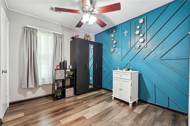 bedroom featuring ceiling fan, visible vents, wood finished floors, and a decorative wall